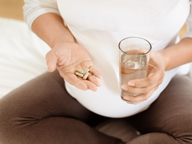 Person holding a handful of vitamins and a glass of water