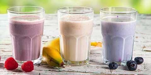 Three protein shakes in glasses with fresh berries and banana