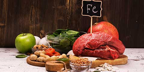 Iron-rich foods including red meat, spinach and legumes beside an Fe sign