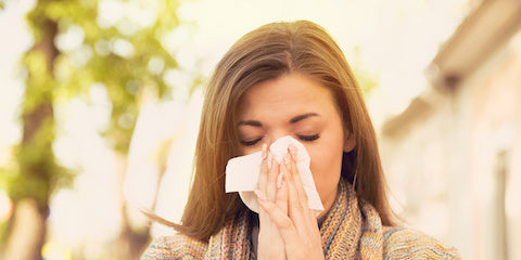 Woman sneezing into a tissue outdoors