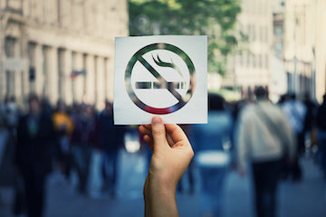 Hand holding a no-smoking sign on a busy city street