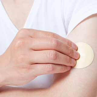 Person applying a round vitamin patch to their upper arm