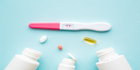 Pregnancy test beside prenatal vitamin bottles on a light blue background