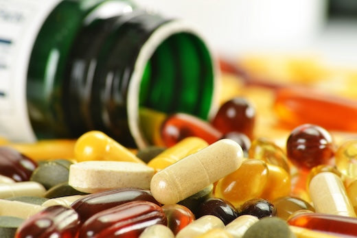 dietary supplements in different colors and shapes lying in front of a supplement bottle on its side