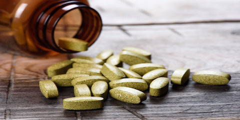 Green softgel supplements spilled from an amber bottle onto a wooden table