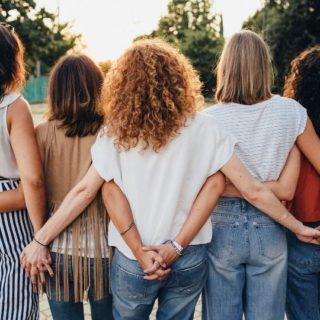 Group of women standing together with arms around each other, seen from behind