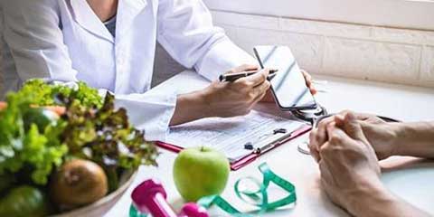 Healthcare provider writing a nutrition plan beside fresh vegetables and an apple