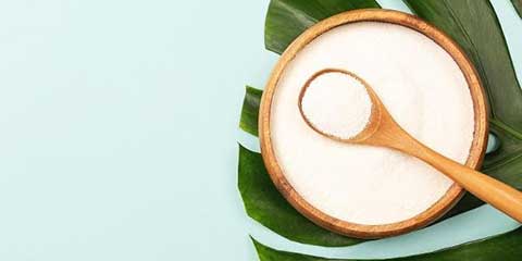 Wooden bowl of collagen powder with a wooden spoon on a green leaf