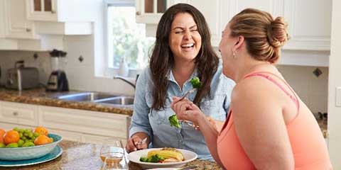 Two women laughing together while cooking in a kitchen