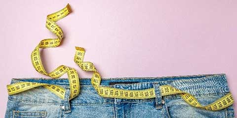 Measuring tape draped over the waistband of a pair of jeans
