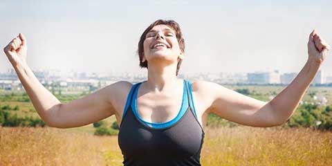 Smiling woman with arms raised outdoors in a sunny field