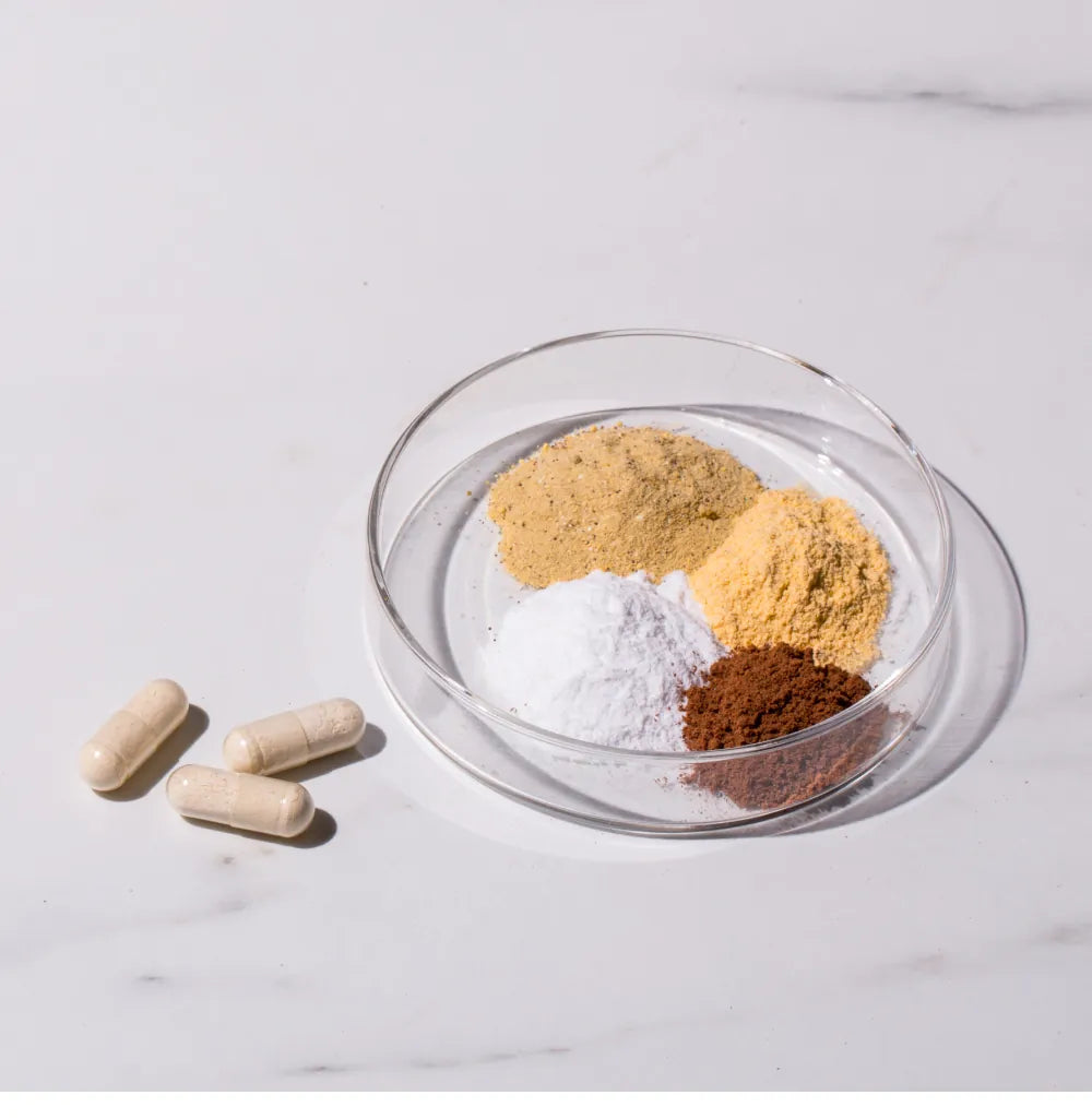 Supplement capsules beside a glass dish of powdered raw ingredients